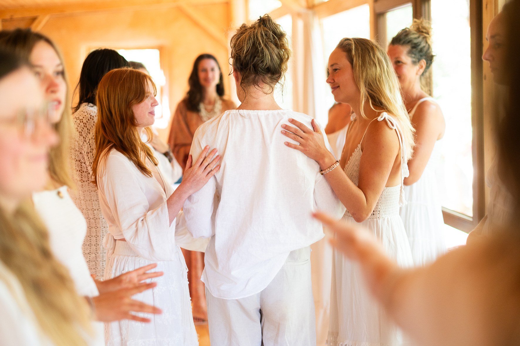 Women in white gathered close, hands on each other's shoulders