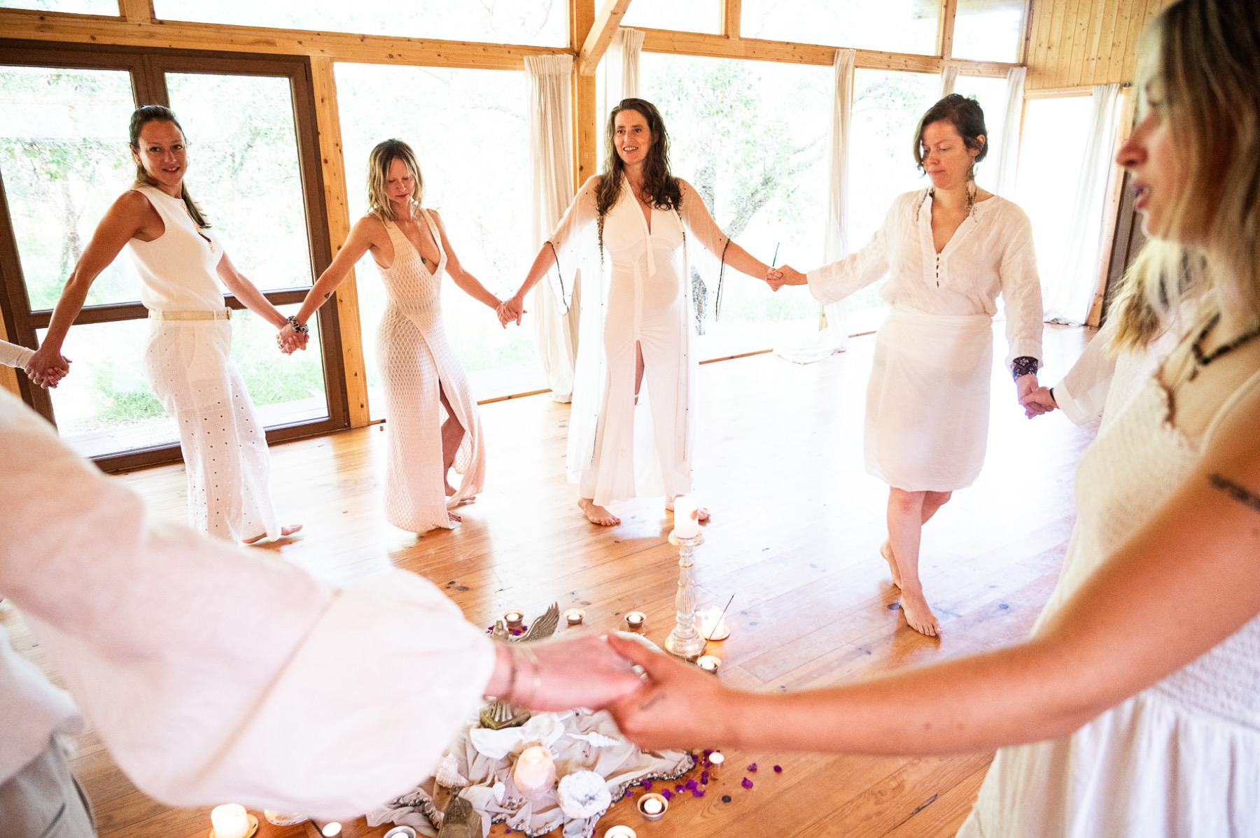Women in white holding hands in a circle around a lit altar