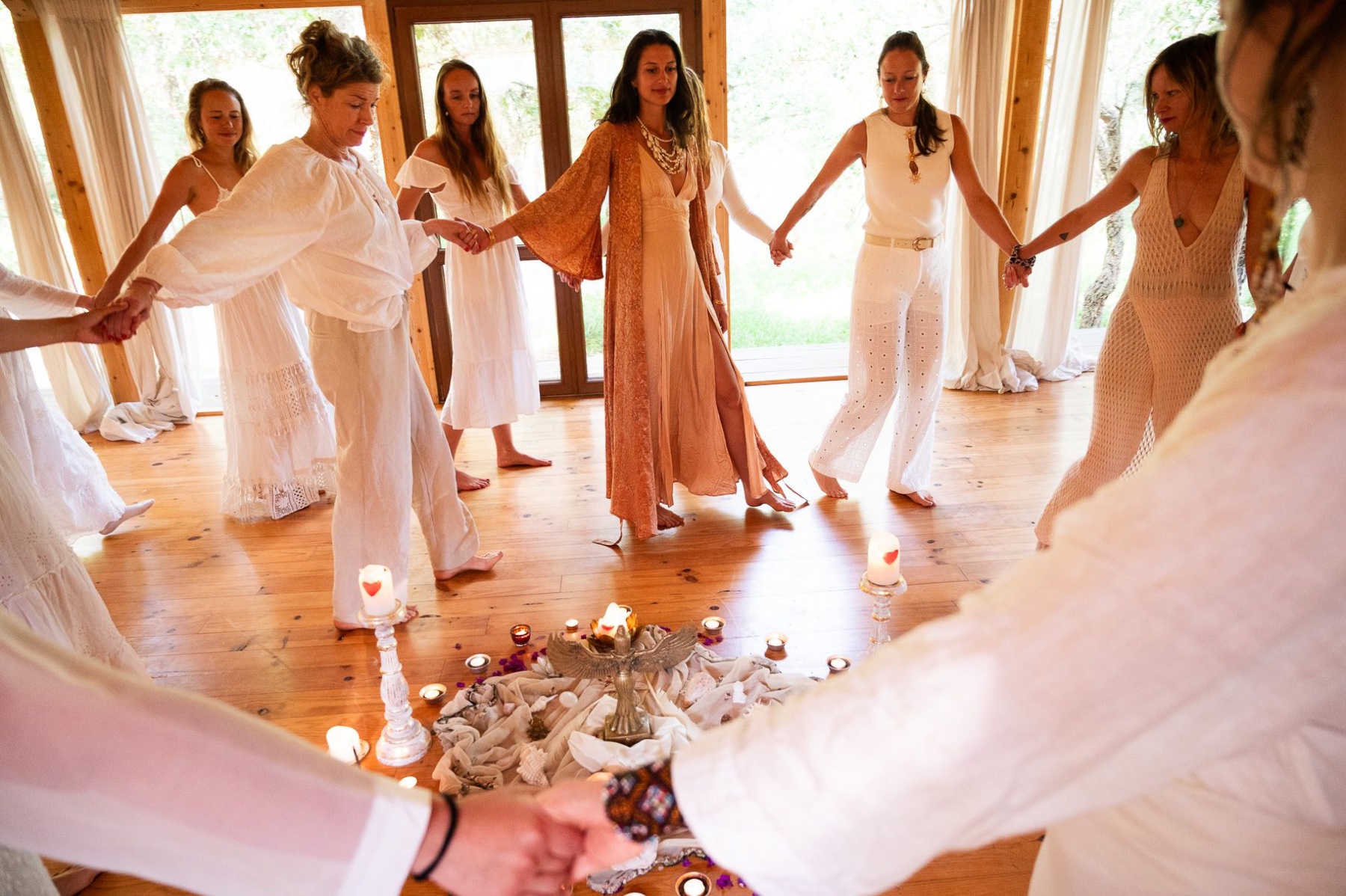 Women holding hands in a ceremonial circle around an altar with candles